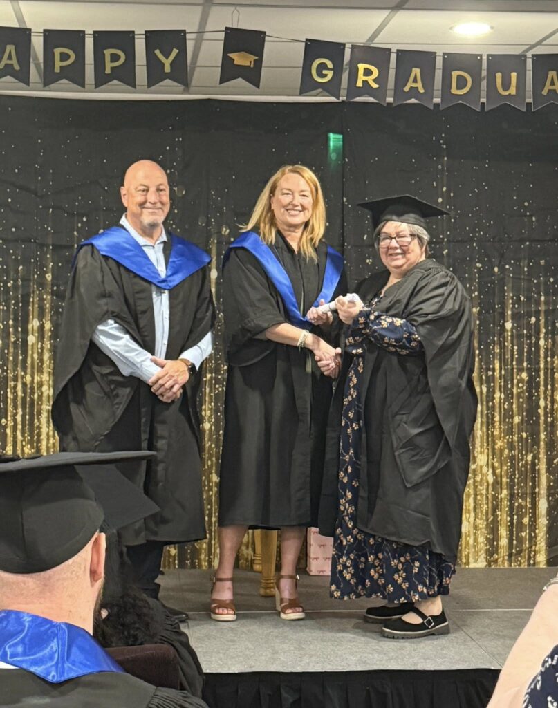 3 people on stage, one of whom is receiving a certificate