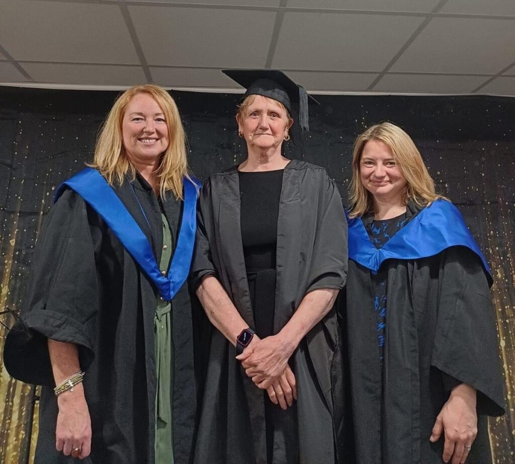 3 people, the middle one wearing cap and gown